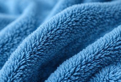 The primary subject of the image is a blue towel with a fuzzy texture. The towel is folded and appears to be made of soft, fluffy material. The setting is a close-up of the towel, showcasing its texture and color. The visual style is a realistic representation of the towel, capturing its details and appearance. The dominant colors in the image are blue and white, creating a calm and soothing atmosphere.