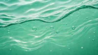 The primary subject of the image is a close-up of a body of water, possibly a lake or a river, with a greenish hue. The water appears to be rippling and has a few bubbles floating on its surface. The setting is outdoors, with the water being the main focus of the scene. The visual style of the image is a close-up, which emphasizes the details of the water and its surroundings. The colors and mood of the image are serene and calming,