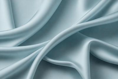 The primary subject of the image is a white sheet of fabric. The setting is a blue background, which creates a contrasting and visually appealing effect. The visual style is a close-up of the fabric, showcasing its texture and details. The colors and mood of the image are predominantly white and blue, giving it a clean and serene atmosphere.