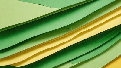 The primary subject of the image is a green and yellow striped paper. The setting is a close-up of the paper, showcasing its vibrant colors and patterns. The visual style is a real-life photograph of the paper. The colors and mood of the image are lively and cheerful, with the green and yellow stripes creating a sense of energy and movement.