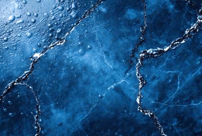 The primary subject of the image is a blue surface with a cracked appearance. The setting is a dark, possibly underwater, environment. The visual style is a close-up of the blue surface, which appears to be a piece of ice or a frozen surface. The colors and mood of the image are predominantly dark and moody, with the blue surface being the main focus.