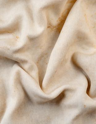 The primary subject of the image is a piece of cloth, possibly a blanket or a sheet, with a dirty and worn appearance. The setting is a close-up view of the cloth, showcasing its texture and appearance. The visual style is a detailed, up-close representation of the cloth, highlighting its worn and dirty state. The colors and mood of the image are predominantly brown and yellow, giving it a somewhat aged and worn look.
