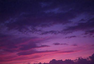 The primary subject of the image is a beautiful sunset with a purple sky. The setting is a cloudy sky, and the visual style is a photo. The colors and mood of the image are predominantly purple, creating a serene and calming atmosphere.