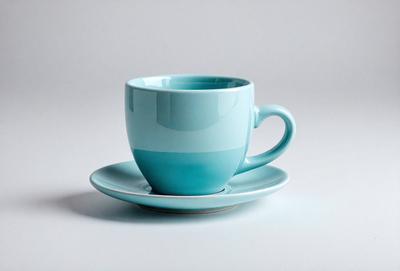 The primary subject of the image is a blue coffee cup placed on a white plate. The setting is a table, and the visual style appears to be a photo. The dominant colors in the image are blue and white, creating a calm and soothing atmosphere.