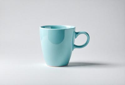 The primary subject of the image is a blue coffee mug. The mug is placed on a white surface, which serves as the background. The visual style of the image is a photo, capturing the details of the mug and its surroundings. The dominant colors in the image are blue and white, creating a calm and soothing atmosphere.