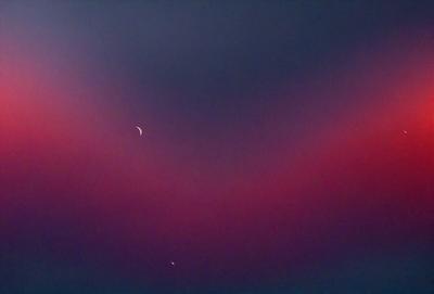 The primary subject of the image is a red sky with a crescent moon visible in the background. The setting is a nighttime scene, and the visual style appears to be a photo. The dominant colors in the image are red and purple, creating a moody and dramatic atmosphere.