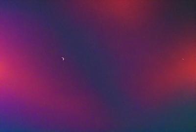 The primary subject of the image is a moon, which is seen in the sky. The setting is a dark, cloudy sky, and the visual style appears to be a photo. The colors and mood of the image are predominantly dark and moody, with the moon being the main source of light in the scene.
