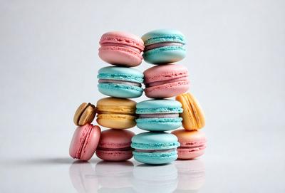 The primary subject of the image is a stack of macarons, which are colorful and visually appealing. The setting is a white background, which provides a clean and minimalist look. The visual style is a close-up of the macarons, showcasing their vibrant colors and intricate designs. The colors and mood of the image are lively and cheerful, with the macarons serving as a delightful centerpiece.