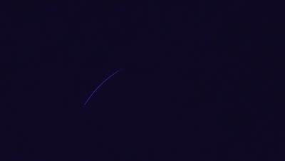 The primary subject of the image is a blue line or streak, which appears to be a rocket or a missile. The setting is a dark, starry night sky, with the blue line extending across the scene. The visual style is a black and white photo, which adds a sense of drama and intensity to the image. The colors and mood of the image are predominantly dark and moody, with the blue line standing out against the black sky.
