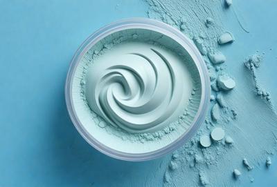 The primary subject of the image is a container of blue cream, which appears to be a type of lotion or cosmetic. The container is placed on a blue surface, which adds to the overall color scheme of the image. The visual style of the image is a close-up of the container, showcasing the cream's texture and color. The dominant colors in the image are blue and white, creating a calm and soothing atmosphere.