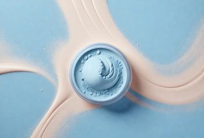 The primary subject of the image is a blue and white makeup container, which is placed on a blue surface. The container is filled with a blue makeup product, which appears to be a cream or a powder. The setting is a blue table, and the visual style is a close-up of the makeup container. The colors and mood of the image are predominantly blue, creating a calm and soothing atmosphere.