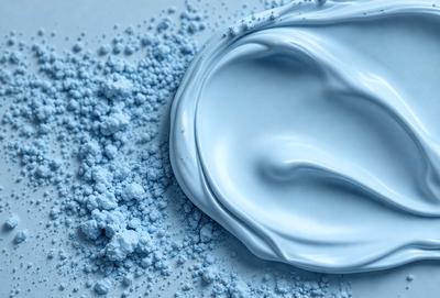The primary subject of the image is a blue substance, which appears to be a creamy or frothy substance. The setting is a white surface, which provides a clean and contrasting background. The visual style of the image is a close-up, focusing on the blue substance. The colors and mood of the image are predominantly blue, creating a calm and soothing atmosphere.