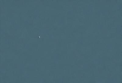 The primary subject of the image is a small planet or moon, which is located in the middle of the sky. The setting is a vast, dark blue sky, with no clouds or other objects visible. The visual style of the image is a photo, capturing the beauty of the celestial object against the backdrop of the night sky. The colors and mood of the image are predominantly dark and serene, with the small planet or moon being the focal point of the scene.