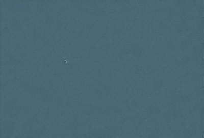 The primary subject of the image is a small planet or moon, which is located in the middle of the scene. The setting is a vast, dark blue sky, with no visible land or other objects. The visual style appears to be a photo, as it captures the natural appearance of the planet in its surroundings. The colors and mood of the image are predominantly dark and moody, with the blue sky and the small planet being the main focus.