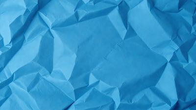 The primary subject of the image is a blue piece of paper with a pattern of folded edges. The setting is a blue background, and the visual style appears to be a close-up of the paper. The colors and mood of the image are predominantly blue, creating a calm and serene atmosphere.