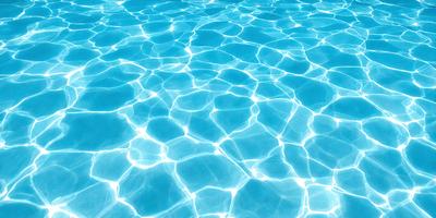 The primary subject of the image is a swimming pool filled with water. The pool is blue and has a clear, sparkling appearance. The setting is a backyard, and the visual style is a photo. The colors and mood of the image are bright and refreshing, with the blue water creating a sense of tranquility and relaxation.