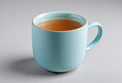 The primary subject of the image is a blue coffee mug filled with tea. The mug is placed on a white surface, which serves as the setting or background. The visual style of the image is a photo, capturing the details of the mug and the tea inside. The dominant colors in the image are blue and white, creating a calm and soothing atmosphere.
