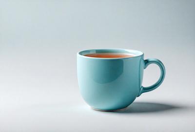 The primary subject of the image is a blue coffee mug filled with tea. The mug is placed on a white surface, which serves as the setting or background. The visual style of the image is a photo, capturing the details of the mug and its contents. The dominant colors in the image are blue and white, creating a calm and soothing atmosphere.