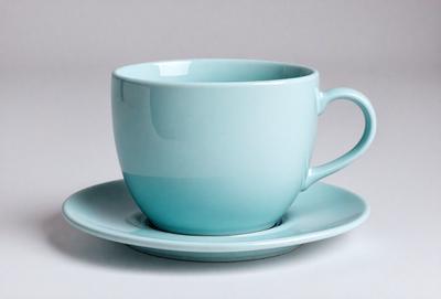 The primary subject of the image is a blue coffee cup placed on a white surface. The cup is positioned on a small plate, which is resting on a larger plate. The setting appears to be a simple and clean environment, with no additional objects or distractions. The visual style of the image is a close-up of the coffee cup, emphasizing its color and shape. The dominant colors in the image are blue and white, creating a calm and soothing atmosphere.