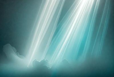 The primary subject of the image is a light source, possibly a sun or a light bulb, shining through a curtain or a piece of fabric. The setting is a dark room, and the visual style appears to be a combination of a photo and a digital art or illustration. The colors in the image are predominantly blue, and the overall atmosphere is serene and calming.