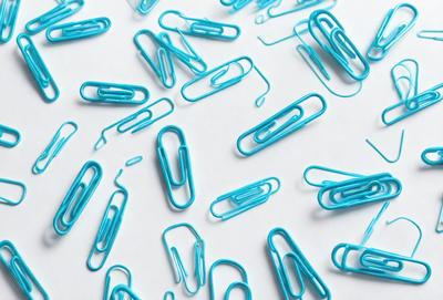 The primary subject of the image is a collection of blue and white office supplies, including many blue and white pins and clips. The setting is a white background, which provides a clean and uncluttered look. The visual style is a close-up of the office supplies, showcasing their colors and details. The overall atmosphere is organized and professional, with the blue and white color scheme adding a touch of elegance to the scene.