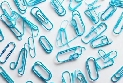 The primary subject of the image is a collection of blue and white office supplies, including various types of clips and pins. The setting is a white background, which provides a clean and uncluttered look. The visual style is a close-up of the office supplies, showcasing their colors and details. The overall atmosphere is organized and professional, as the supplies are neatly arranged and displayed.