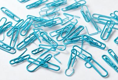 The primary subject of the image is a collection of blue paper clips. The setting is a white surface, which provides a clean and uncluttered backdrop for the clips. The visual style is a close-up of the paper clips, showcasing their vibrant blue color and the intricate details of their design. The overall atmosphere of the image is organized and professional, with the blue paper clips serving as a functional and decorative element.