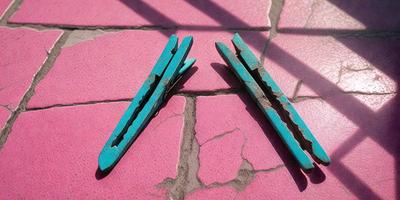 The primary subject of the image is a pair of blue scissors. The scissors are placed on a pink surface, which could be a table or a counter. The setting appears to be a room with a window, providing natural light. The visual style of the image is a photo, capturing the details of the scissors and the pink surface. The colors in the image are predominantly pink and blue, creating a warm and inviting atmosphere.