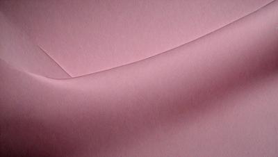 The primary subject of the image is a pink sheet of paper. The setting is a room with a pink background. The visual style is a close-up of the pink paper, showcasing its texture and color. The colors and mood of the image are predominantly pink, creating a warm and inviting atmosphere.