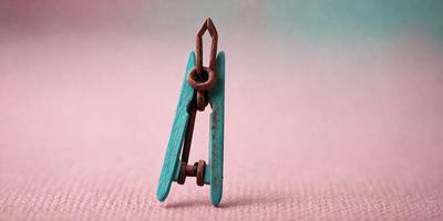 The primary subject of the image is a wooden clothespin with a chain hanging from it. The setting is a pink surface, which serves as the background. The visual style is a close-up of the clothespin, showcasing its details. The colors in the image are predominantly pink, giving the scene a warm and inviting atmosphere.