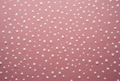 The primary subject of the image is a close-up of a pink surface with white dots on it. The setting appears to be a room with a pink wall, and the visual style is a patterned texture. The dominant colors are pink and white, creating a warm and inviting atmosphere.