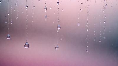 The primary subject of the image is a series of droplets of water hanging from strings. The setting is a cloudy sky, and the visual style is a photo. The dominant colors are shades of pink and purple, creating a warm and serene atmosphere.