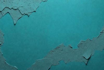 The primary subject of the image is a blue wall with peeling paint. The setting is a room with a blue background. The visual style is a close-up of the peeling paint, which gives the image a textured and artistic appearance. The dominant colors are blue and white, creating a calm and soothing atmosphere.