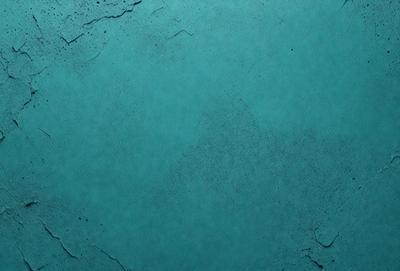 The primary subject of the image is a large, blue wall with a rough texture. The setting is a room with a blue-green color scheme. The visual style is a close-up of the wall, showcasing its unique texture. The colors and mood of the image are predominantly blue and green, creating a calm and serene atmosphere.