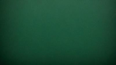 The primary subject of the image is a large, green, textured surface. The setting is a dark room, and the visual style appears to be a photo. The dominant colors are green and black, creating a moody atmosphere.