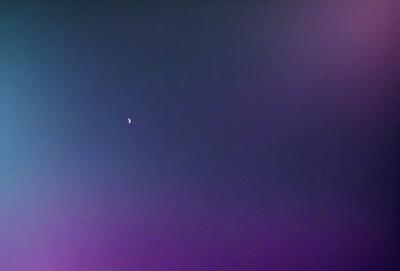 The primary subject of the image is a moon, which is seen in the sky. The setting is a dark, cloudy night sky, with the moon being the main focus. The visual style of the image is a photo, capturing the moon in its natural environment. The colors and mood of the image are predominantly dark and moody, with the moon being the only bright spot in the sky.