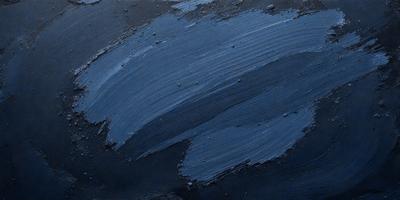 The primary subject of the image is a blue paint splatter on a black surface. The setting appears to be an artistic or creative environment, possibly a painting or drawing studio. The visual style of the image is a close-up of the blue paint splatter, showcasing the details of the paint and the black surface. The colors and mood of the image are predominantly blue and dark, creating a moody and artistic atmosphere.