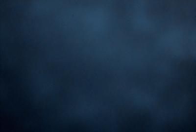 The primary subject of the image is a dark blue sky with a few clouds. The setting is a vast, open space with no visible landmarks or objects. The visual style is a natural, outdoor scene. The colors and mood are predominantly dark and moody, with the blue sky and clouds creating a sense of depth and vastness.