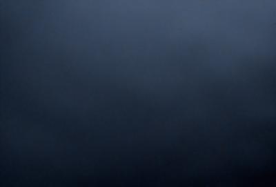 The primary subject of the image is a dark, cloudy sky. The setting is a vast, open space with no visible landmarks or objects. The visual style is a black and white photo, which adds a sense of depth and contrast to the scene. The colors and mood of the image are predominantly dark and moody, with the clouds and sky creating a dramatic atmosphere.