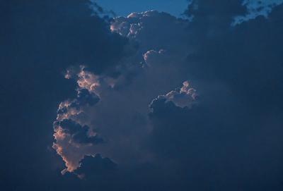 The primary subject of the image is a cloudy sky with a large cloud in the center. The setting is an outdoor environment, and the visual style appears to be a photo. The cloudy sky has a dark and moody atmosphere, with the large cloud dominating the scene.