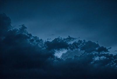 The primary subject of the image is a cloudy sky with a blue hue. The setting is a nighttime scene, with the sky being the main focus of the image. The visual style is a photo, capturing the beauty of the cloudy sky. The colors and mood of the image are predominantly blue, creating a serene and peaceful atmosphere.