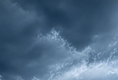 The primary subject of the image is a cloudy blue sky. The setting is a vast expanse of the sky, with no visible land or other objects. The visual style is a natural, outdoor scene. The colors and mood are predominantly blue and calm, with the clouds creating a sense of depth and tranquility.