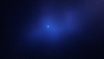 The primary subject of the image is a bright star, which is the main focus of the scene. The setting is a dark, cloudy sky, creating a dramatic backdrop for the star. The visual style of the image is a photo, capturing the star's light and the surrounding darkness. The colors in the image are predominantly dark, with the star being the brightest point of light, creating a moody atmosphere.