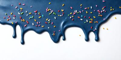 The primary subject of the image is a blue surface with a drizzle of chocolate sauce and sprinkles on it. The setting appears to be a white background, and the visual style is a combination of a photo and digital art. The colors and mood of the image are predominantly dark, with the blue surface contrasting against the chocolate and sprinkles.