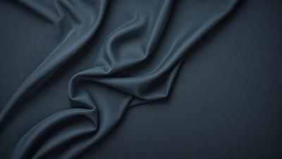 The primary subject of the image is a blue fabric, which is the main object, scene, or focus of the image. The setting or background is a dark blue surface, which provides a contrasting backdrop for the fabric. The visual style of the image is a close-up of the fabric, showcasing its texture and details. The colors and mood of the image are predominantly dark blue, creating a calm and serene atmosphere.