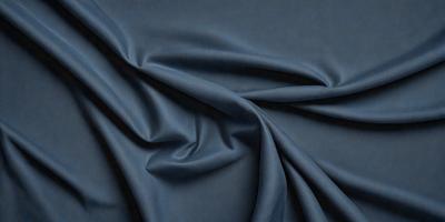 The primary subject of the image is a blue fabric, which is the main object, scene, or focus of the image. The setting or background is a dark blue surface, and the visual style is a close-up of the fabric. The colors and mood of the image are predominantly dark blue, creating a moody and dramatic atmosphere.
