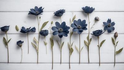 The primary subject of the image is a row of blue flowers, which are arranged in a vase. The flowers are placed on a white wall, creating a visually appealing contrast between the blue flowers and the white background. The visual style of the image is a photo, capturing the beauty of the flowers in their natural setting. The colors and mood of the image are predominantly blue, giving it a calm and serene atmosphere.