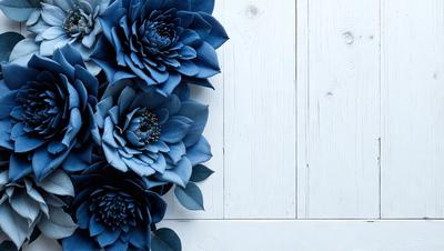 The primary subject of the image is a bouquet of blue flowers, which are arranged in a vase. The flowers are placed on a white wooden table, creating a contrast between the blue flowers and the white background. The visual style of the image is a close-up of the flowers, showcasing their details and beauty. The colors and mood of the image are predominantly blue, giving it a calm and serene atmosphere.