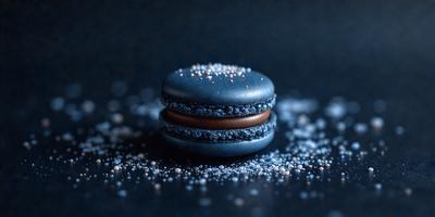 The primary subject of the image is a close-up of a chocolate and blue macaroon. The setting is a black surface, and the visual style is a photo. The dominant colors are blue and brown, creating a rich and indulgent atmosphere.