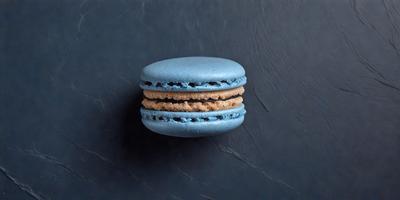 The primary subject of the image is a blue macaroon with a yellow filling, sitting on a grey surface. The setting is a dark background, which contrasts with the vibrant colors of the macaroon. The visual style is a close-up of the macaroon, showcasing its details. The colors and mood of the image are predominantly dark and moody, with the blue and yellow macaroon being the main focal point.